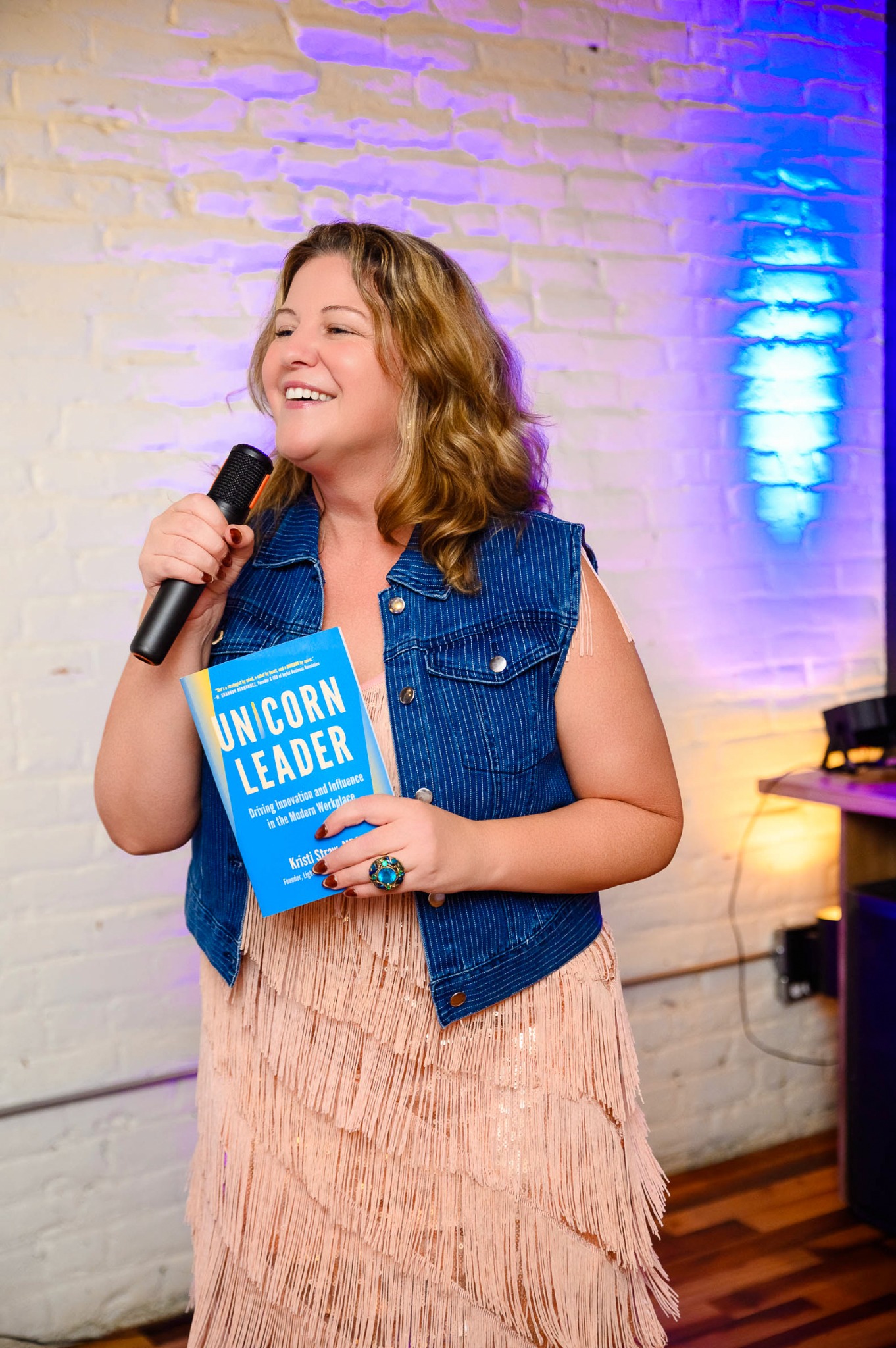 Kristi Straw speaking with a microphone and holding UNICORN Leader